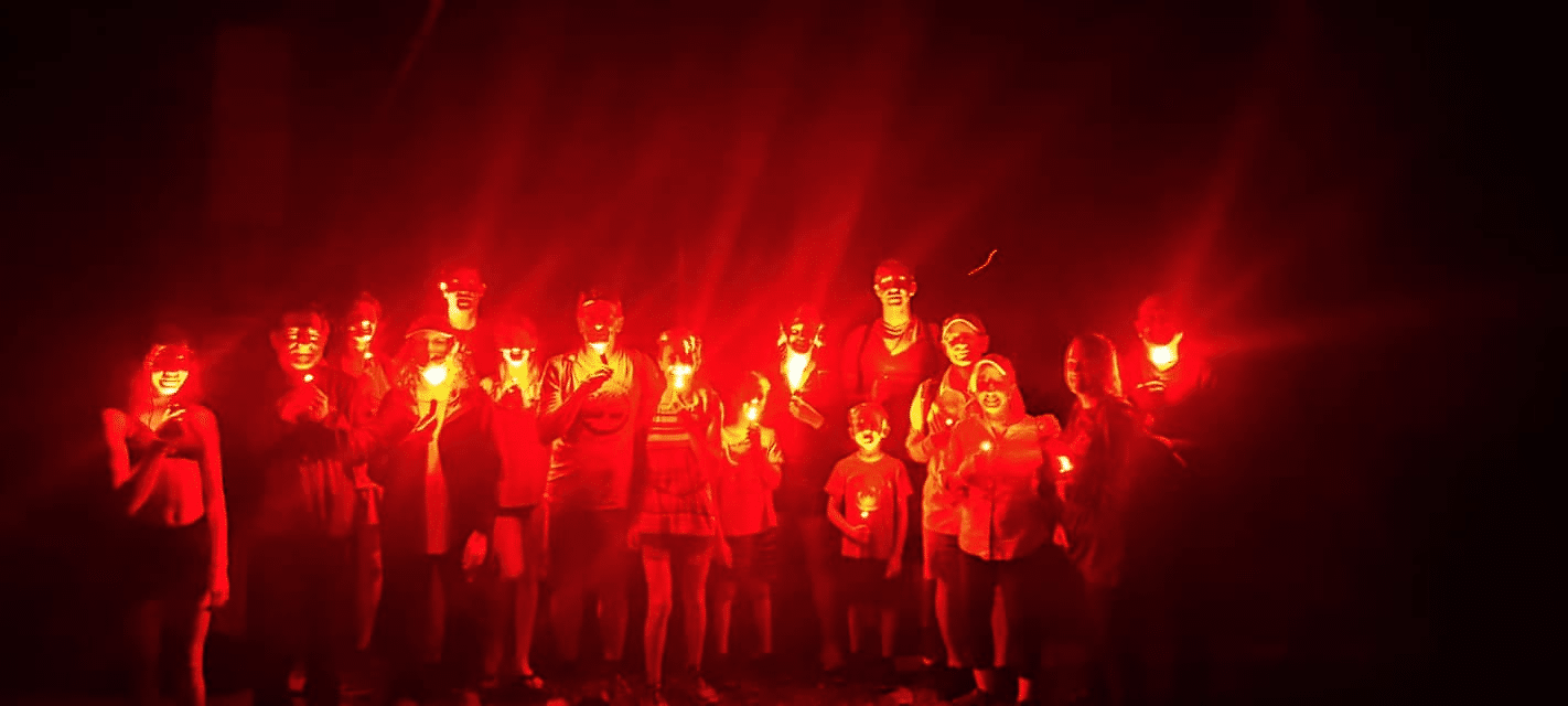 Hikers in the dark illuminated by red lights.
